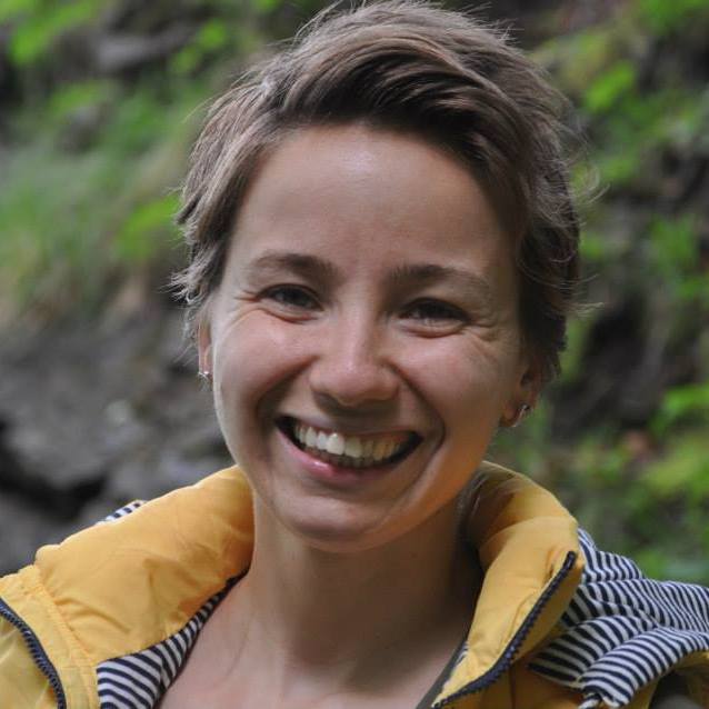 Alecsa Stewart smiling on a green trail in a yellow jacket